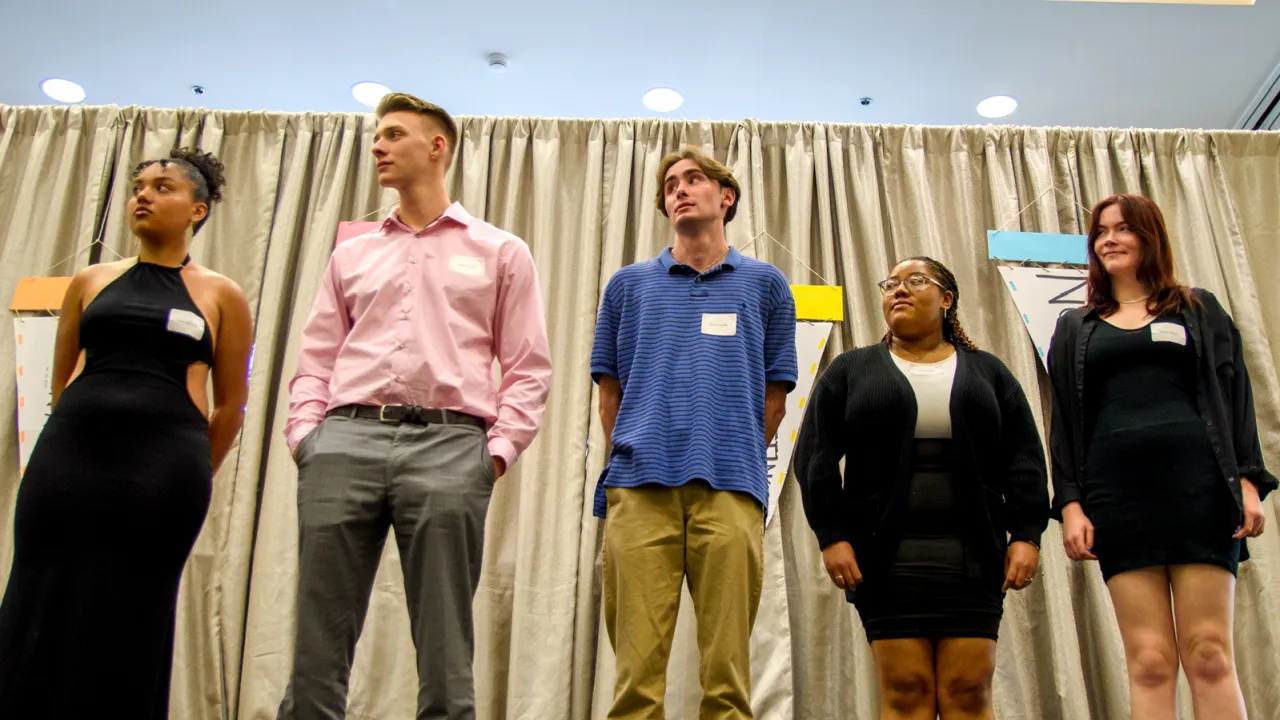 Five students standing on a stage with a gold backdrop.