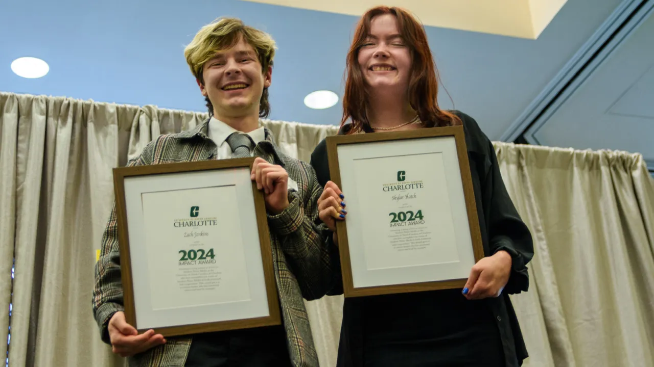  Two people holding up awards in frames, standing in front of a curtain.