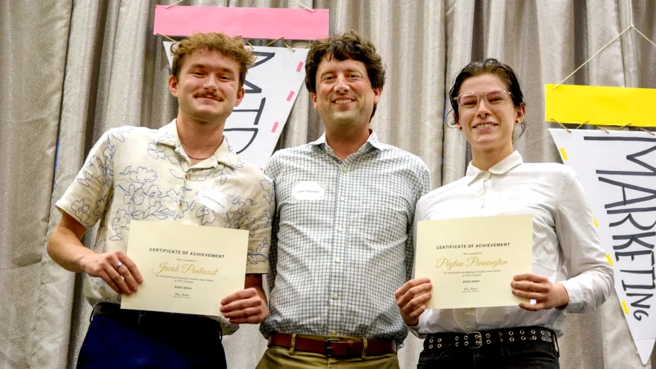 Three individuals posing with certificates in front of a curtain backdrop