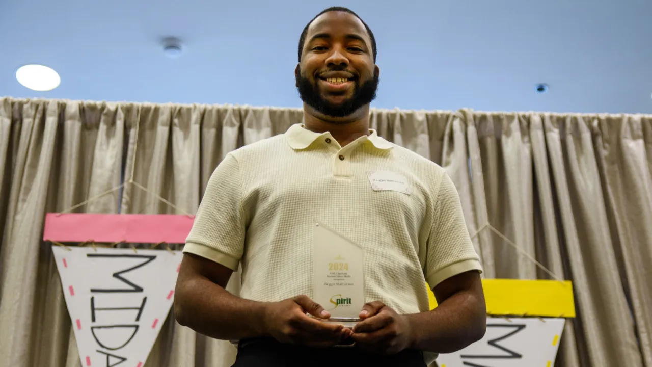 A student proudly holds an award in front of a banner