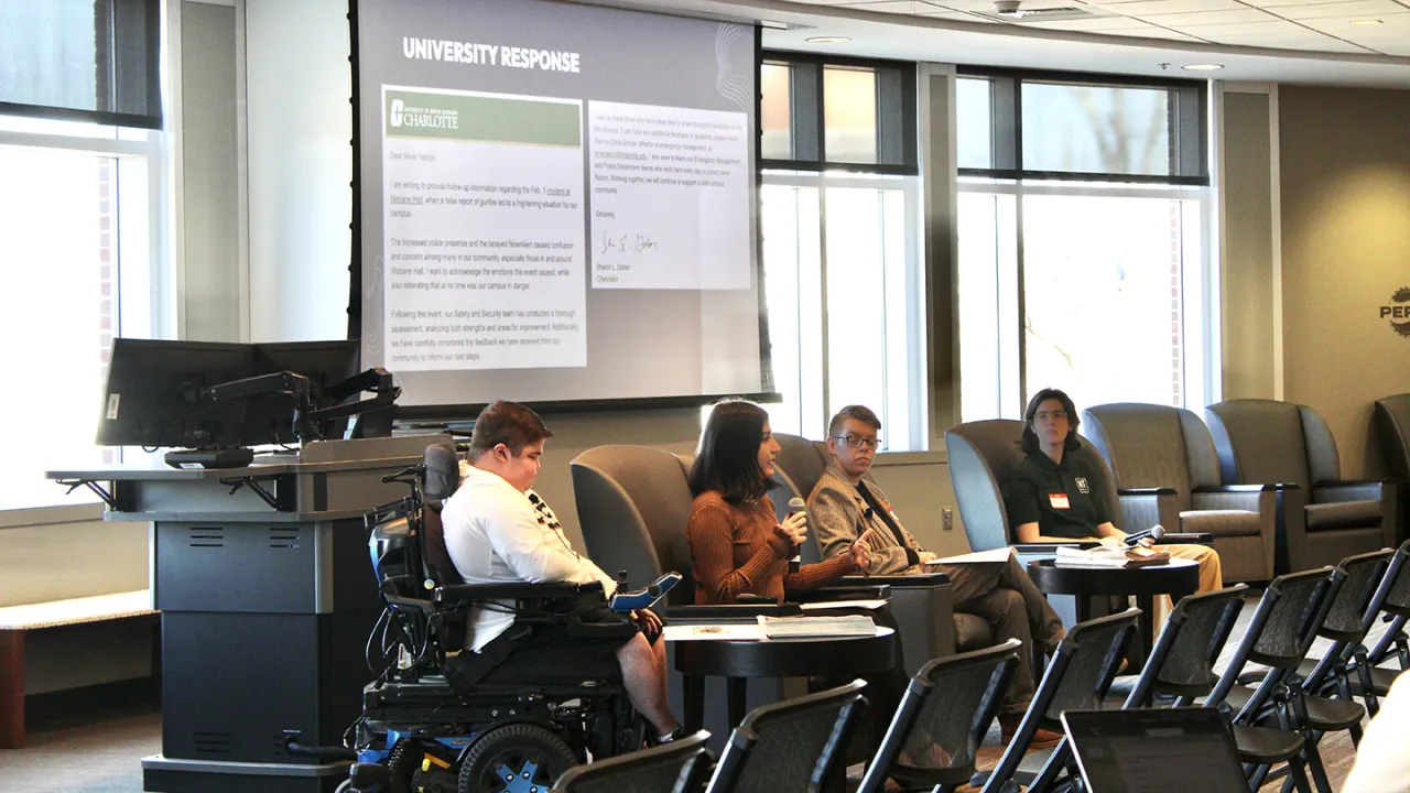 Panelists seated at a table in front of a presentation screen with the title "university response" in a conference room setting.