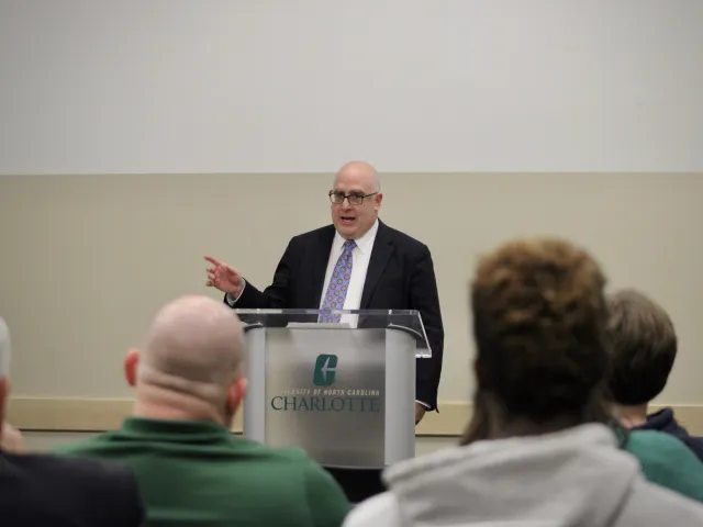 A man in a suit and tie delivering a speech to a crowd of people, capturing their attention and engagement.